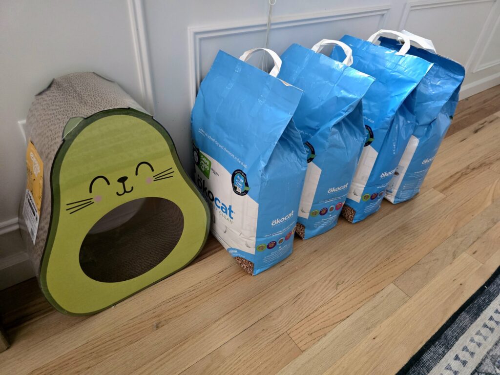 Four bags of cat litter and scratching post showing bringing cat to college supply preparation and bulk shopping strategies