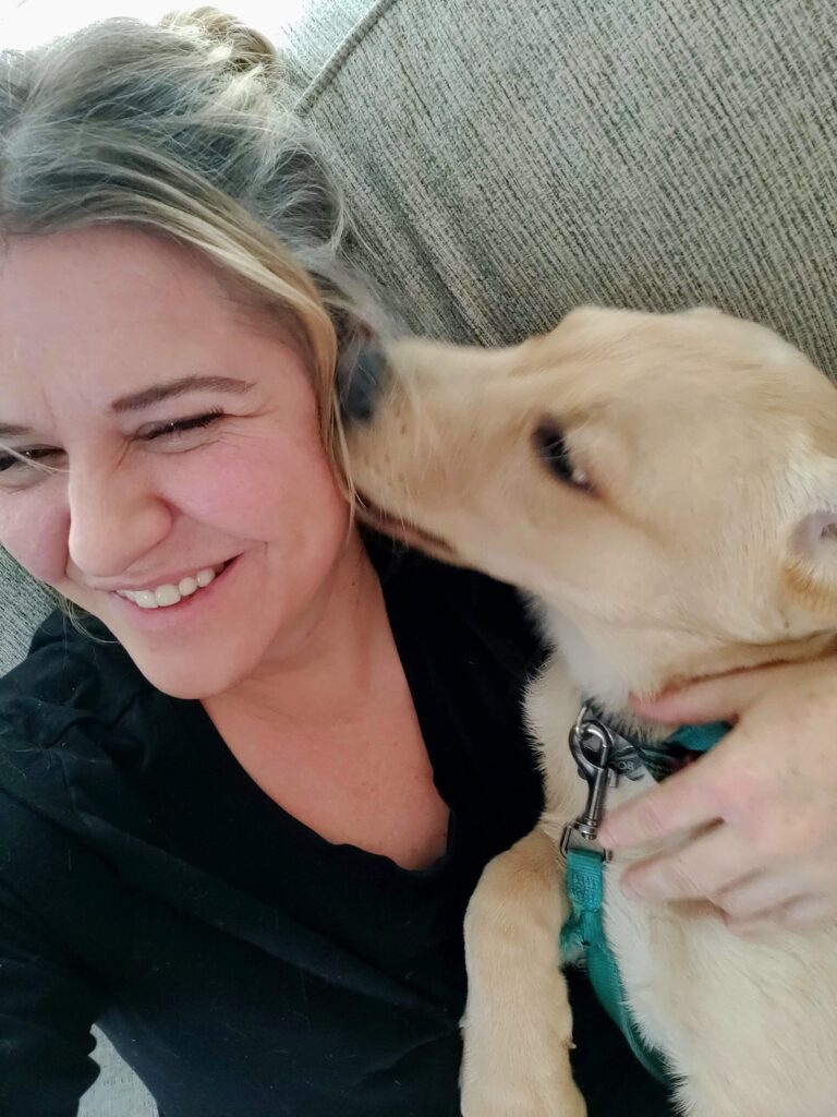 Yellow Labrador puppy kissing his ownerโs cheek while cuddling on the couch, showing physical affection as part of a dogโs love language.